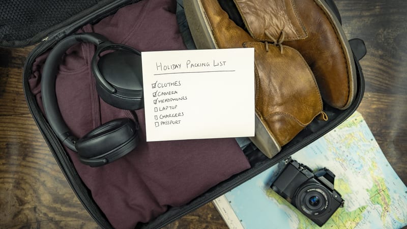 Open suitcase with a handwritten packing list, headphones, camera and chargers ready for an overseas trip